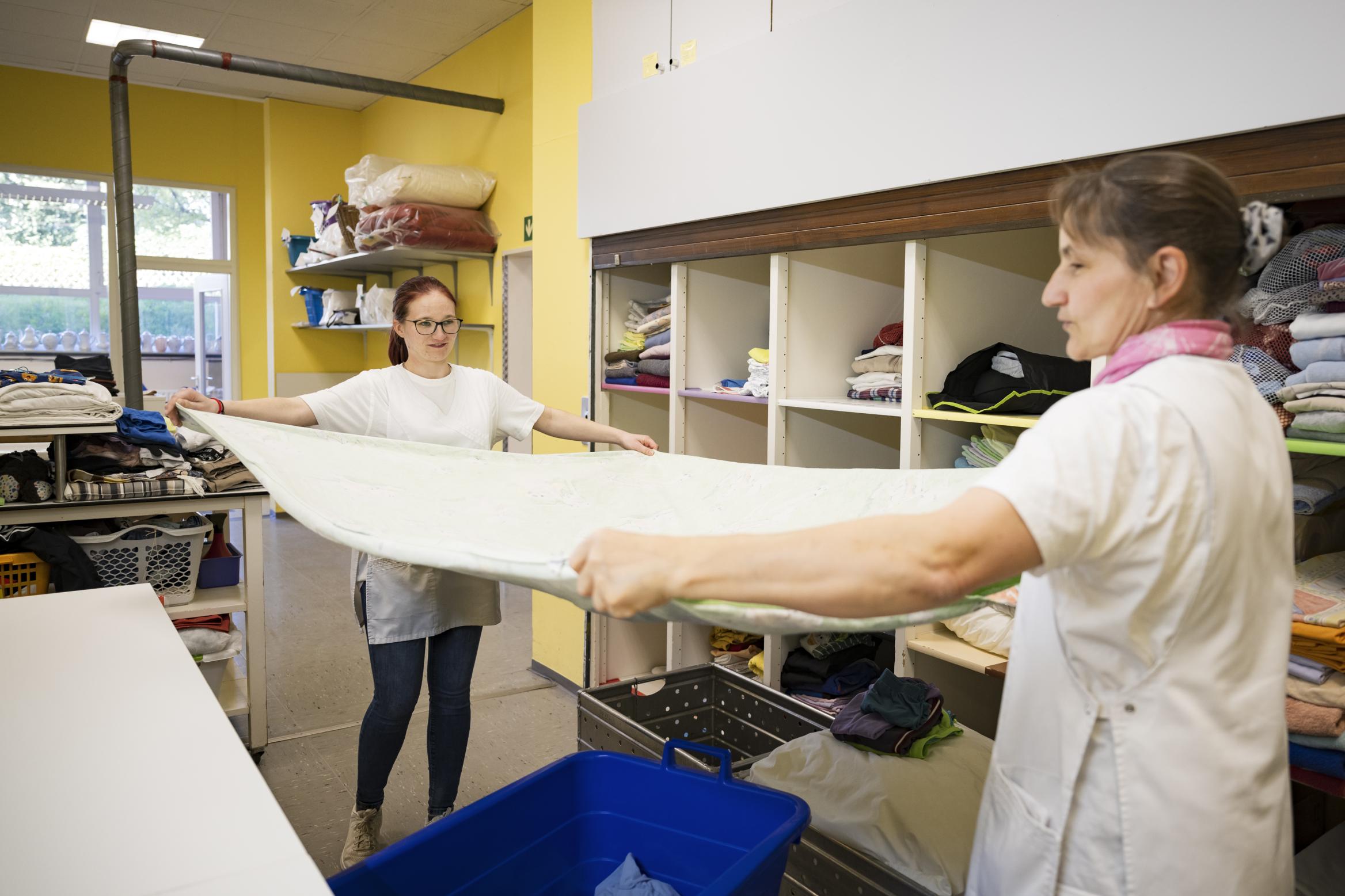 zwei Frauen glätten ein Tischtuch in einer Wäscherei