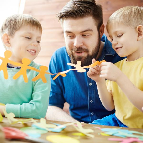 zwei Kinder basteln mit ihrem Vater Papiergirlanden