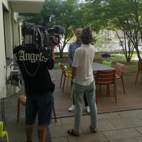 Kameramann und Reporterin im Innenhof mit Vorstand vor Bäumen