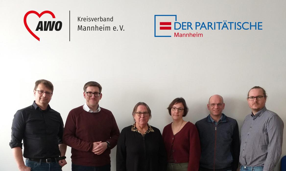 mehrere Menschenstehen  vor einer hellen Wand