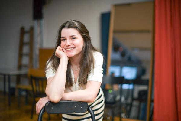 junge Frau stützt sich mit dem Ellenbogen auf eine Stuhllehne und lacht 