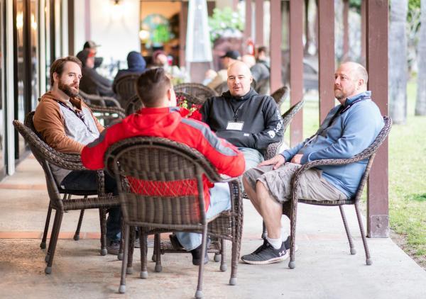 kleine Gruppe von m&auml;nnlich gelesenen Personen sitzt im Kreis um einen Tisch und unterh&auml;lt sich