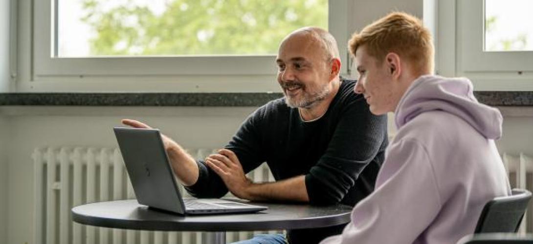 ein junger Mann schaut einem Berater an einem Tisch in einen Laptop