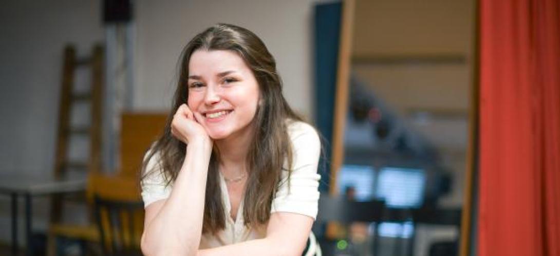 junge Frau stützt sich mit dem Ellenbogen auf eine Stuhllehne und lacht 