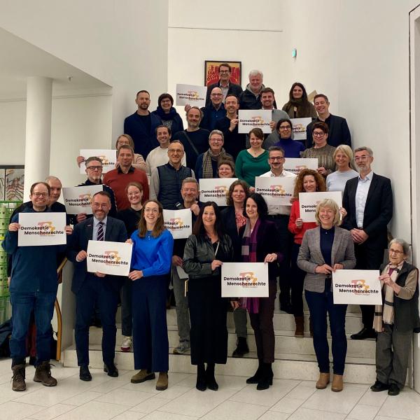 Männer und Frauen auf einer Treppe, die Schilder "Demokratie und Menschenrechte" hochhalten