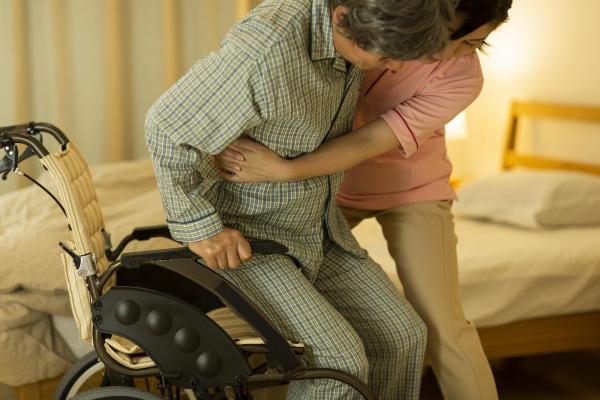 Pflegekraft hilft Frau ins Bett