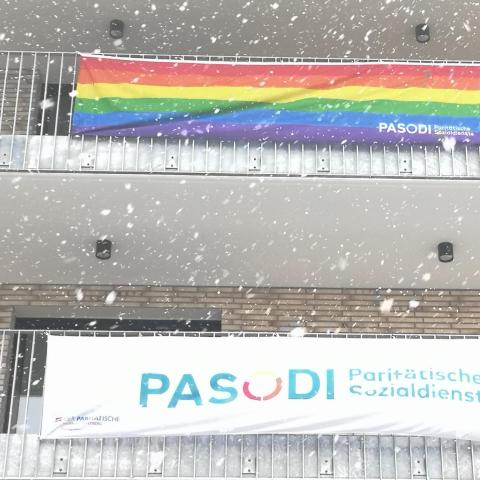 an einem Balkon hängen die Regenbogen und die PASODI Flagge